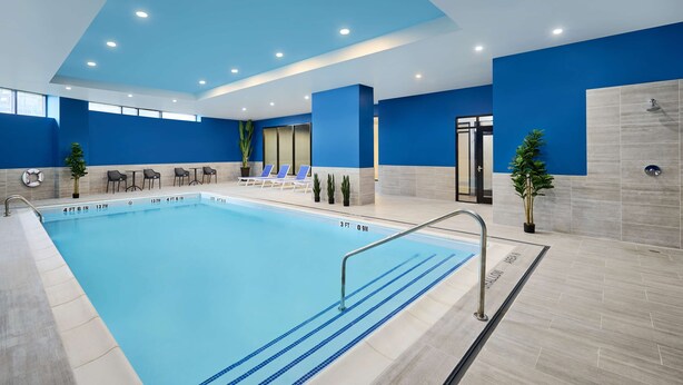 A modern indoor swimming pool with clear lane markings, a lifeguard chair, and lounge chairs. - Hampton Inn by Hilton Hamilton (Hamilton)