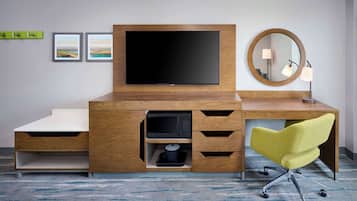 A hotel room with a wooden desk, a flat-screen TV, a yellow office chair, a microwave, and a small sink.