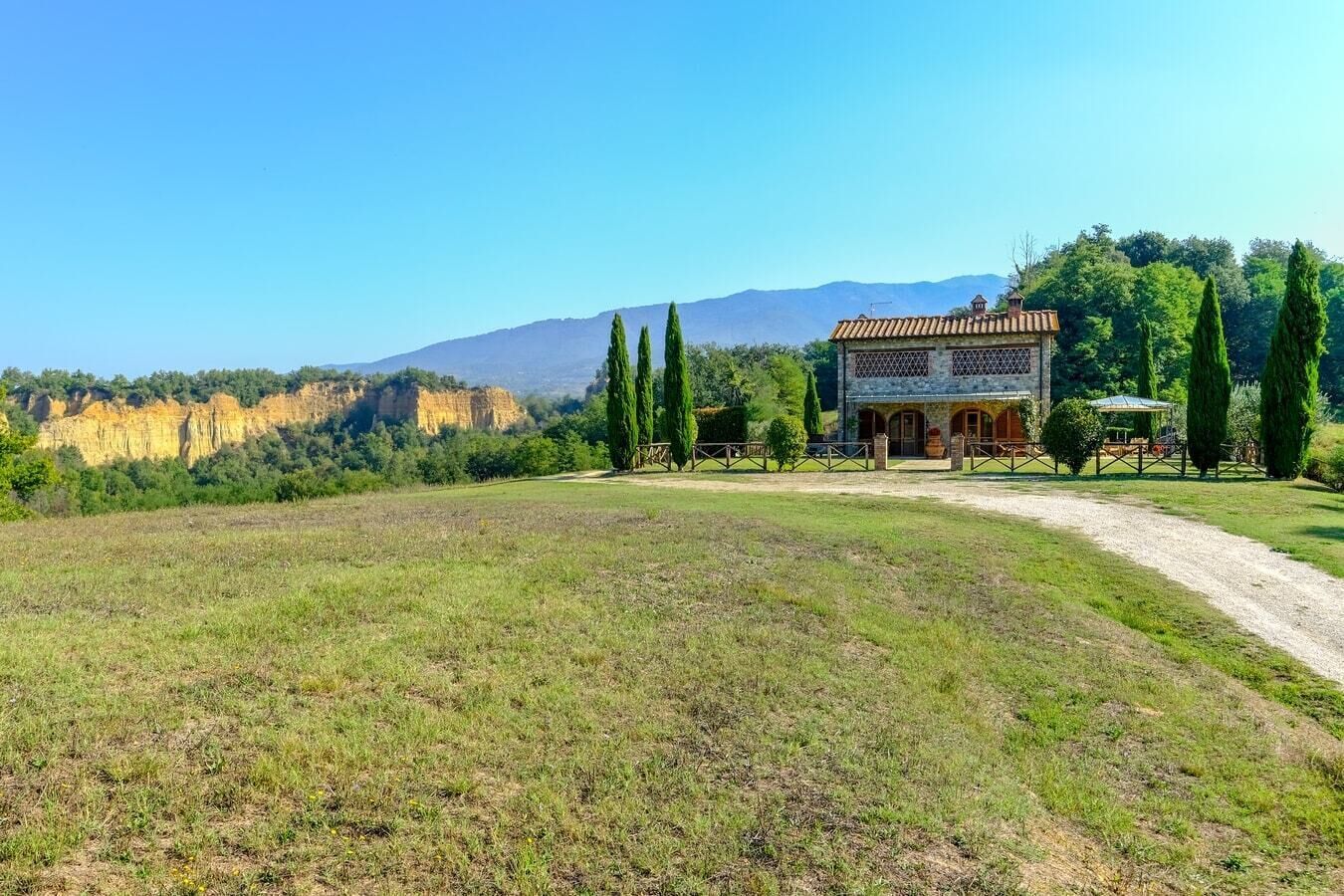 A rustic villa with a stone facade, arched windows, and a gravel driveway leading to a wooden deck.