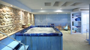 A spa area with a hot tub, stone wall, wooden steps, and a blue color scheme.
