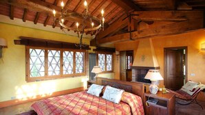 A bedroom with a large bed, a fireplace, and a wooden ceiling.
