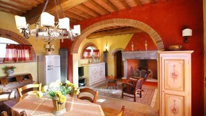 A dining area with a wooden table, chairs, and a chandelier. There is a fireplace and a cabinet with decorative items.