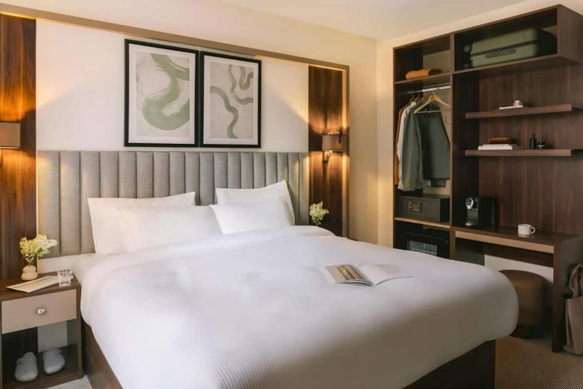 A neatly arranged hotel room with a large bed, a wardrobe, and a bedside table with a lamp.