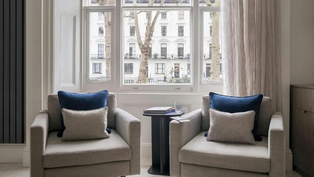 A room with two armchairs facing a window with a view of buildings. - The Voyage Hotel Paddington  (London)