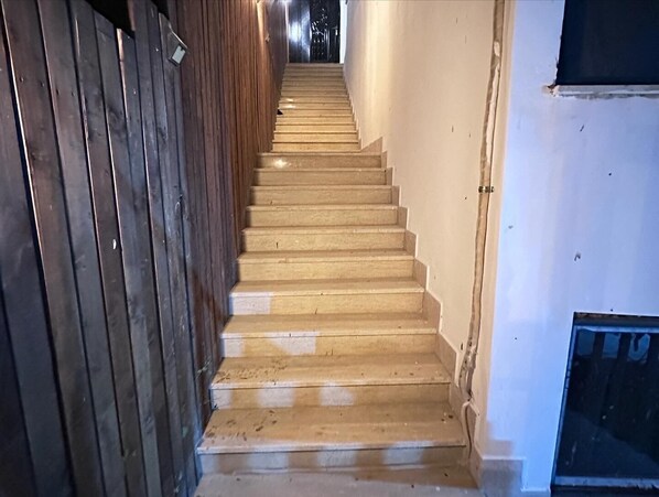 Una escalera de madera con peldaños que ascienden, flanqueada por un muro de madera a un lado y una pared blanca al otro.
