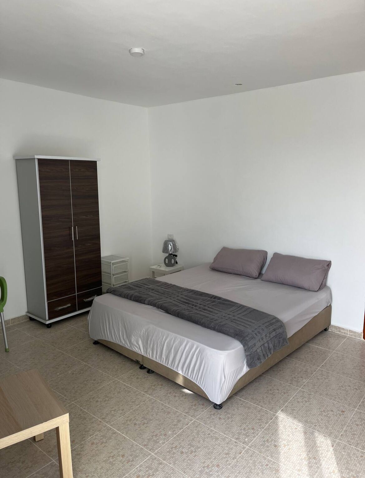 A bedroom with a bed, a wardrobe, a bedside table, and a lamp.
