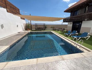 A swimming pool with a tiled pattern, surrounded by lounge chairs and a shaded area.