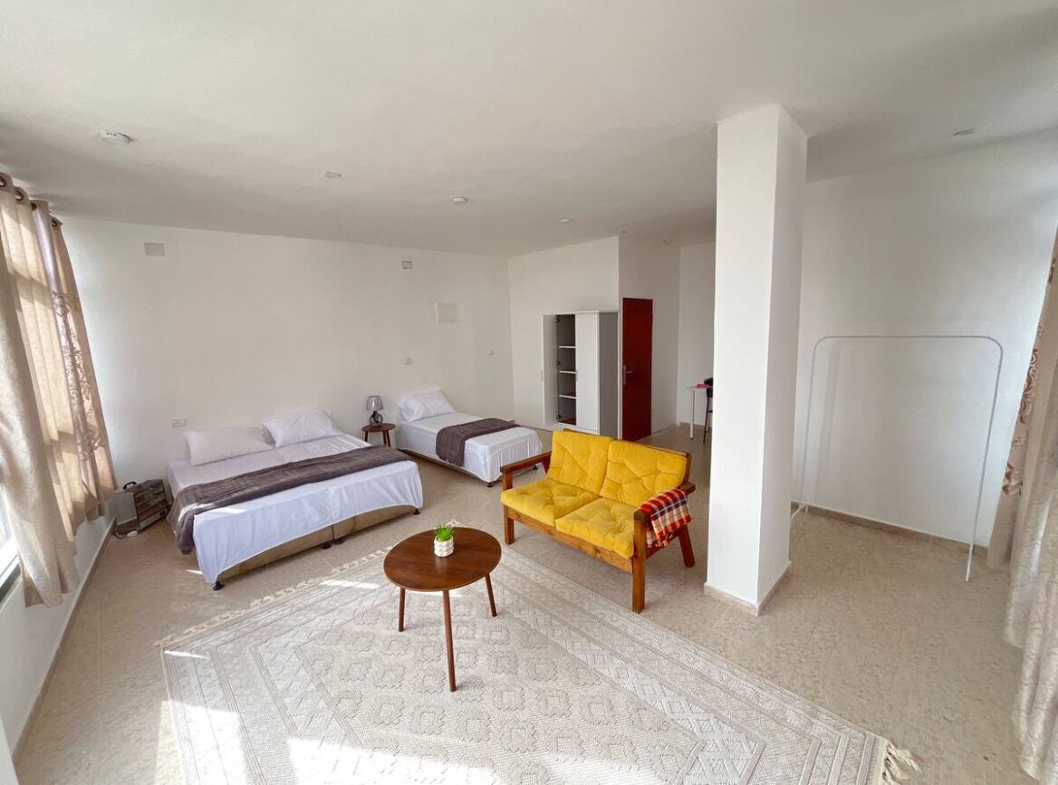 A spacious room with a bed, a sofa, a small table, and a wardrobe.