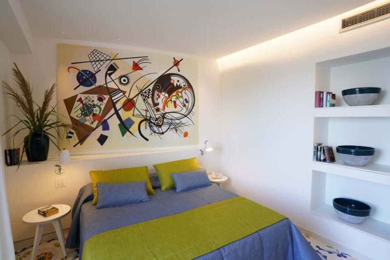 Ein modernes Schlafzimmer mit einem Bett, einem farbenfrohen abstrakten Gemälde, einer Topfpflanze und Regalen mit Schalen.