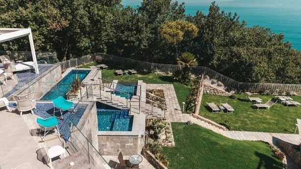 Un espace piscine sur le toit, comprenant plusieurs piscines, des chaises longues et une vue sur la mer et les montagnes.