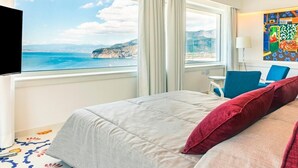 Une chambre d’hôtel équipée d’un lit, d’une télévision, d’un bureau, d’une chaise et offrant une vue sur la mer et les falaises.