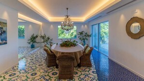 Un coin repas avec une table ronde et des chaises en osier, un lustre et un sol à motifs.