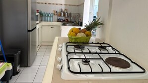 A kitchen with a gas stove, a refrigerator, and a fruit bowl on the counter. - A 8mn de la Plage, T2 Situé au Centre de Sainte-anne Guadeloupe (SAINTE-ANNE)