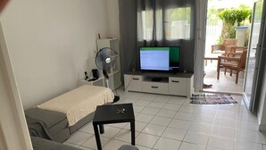 A compact living space with a sofa, a small table, a TV, and a fan. - A 8mn de la Plage, T2 Situé au Centre de Sainte-anne Guadeloupe (SAINTE-ANNE)