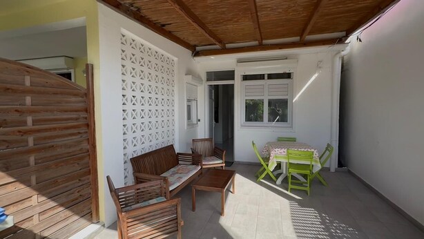 A covered patio with wooden furniture, a white wall with a lattice design, and a window. - A 8mn de la Plage, T2 Situé au Centre de Sainte-anne Guadeloupe (SAINTE-ANNE)