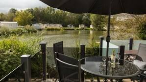 En matplats med ett bord och stolar, ett parasoll och utsikt över en sjö med hus i bakgrunden.