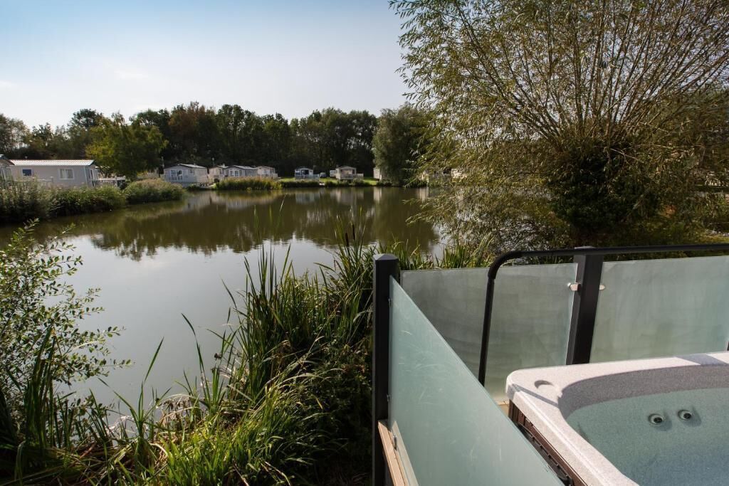 Un cadre extérieur paisible, avec un plan d’eau, un jacuzzi et, au loin, une rangée de maisons mobiles.