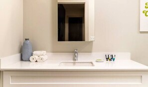 Un bany amb un lavabo blanc, un mirall, un suport per a tovalloles amb tovalloles, un ram i productes de tocador.