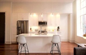 A modern kitchen with white cabinetry, stainless steel appliances, and pendant lighting.