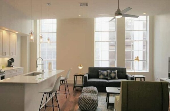 A modern kitchen with a central island, bar stools, a sofa, and a dining area.