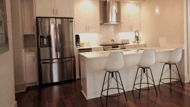 A modern kitchen with stainless steel appliances, a central island with bar stools, and white cabinetry.