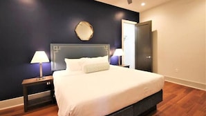 A neatly arranged bedroom with a bed, two bedside tables, a nightstand, a wall-mounted mirror, and a door.