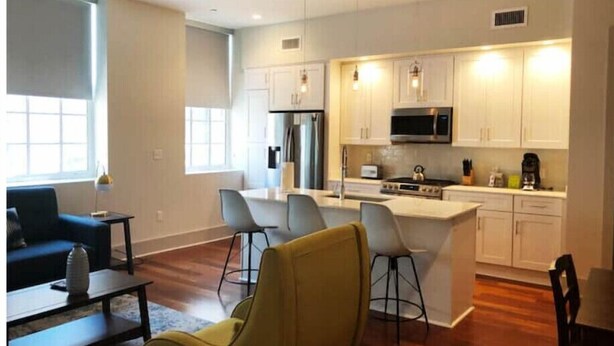 A modern kitchen with white cabinets, a central island, and a dining area with bar stools. - The 820 Unit 302 - 2 BR Walk to Bourbon Street! (New Orleans)