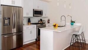 A modern kitchen with white cabinetry, stainless steel appliances, and a central island with bar stools.