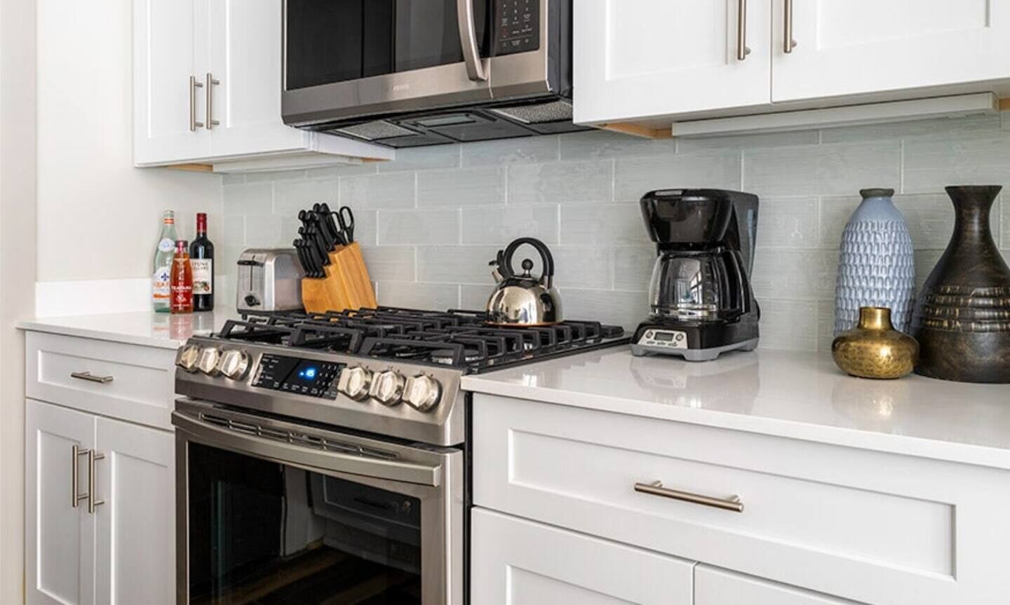 A modern kitchen with white cabinets, a stainless steel stove, a microwave, and a coffee maker.