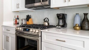 A modern kitchen with white cabinets, a stainless steel stove, a microwave, and a coffee maker. - Close to Hospitals & close to the French Quarter! 2BR Unit 202 (New Orleans)
