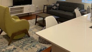 A modern living room with a flat-screen TV, a ceiling fan, a sofa, a dining table, and pendant lights. - Close to Hospitals & close to the French Quarter! 2BR Unit 202 (New Orleans)