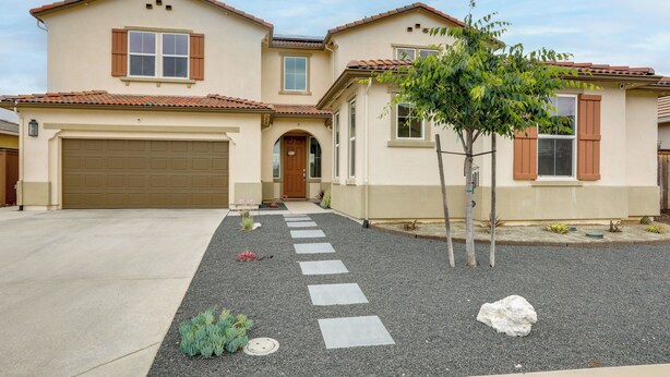 A two-story house with a garage, a front door, and a small tree in the front yard.