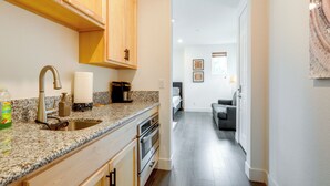 A kitchen with granite countertops, stainless steel appliances, wooden cabinets, and a view into a living area with a gray sofa and a framed picture on the wall.