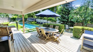 Una terrazza in legno con piscina, mobili da esterno e una zona coperta con ombrellone.
