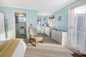 Un dormitorio moderno con una cama grande, una silla, un escritorio y un baño visible a través de una puerta abierta.