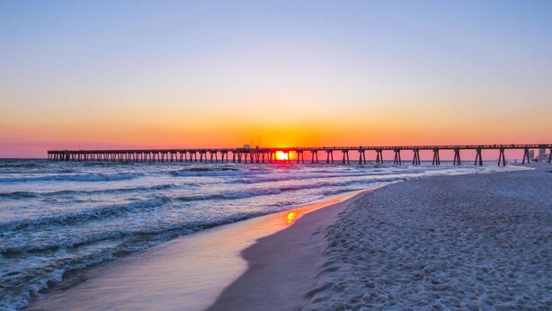 Een strand met een pier die zich uitstrekt over de oceaan bij zonsondergang.
