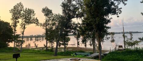 A lakeside picnic area with a wooden table and benches, surrounded by trees and a view of the water.