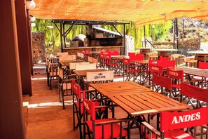 An outdoor dining area with wooden tables and chairs, a grill, and a stone wall. - HOTEL VALLE GRANDE (El Nihuil)