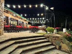 A restaurant with outdoor seating, stone steps leading up to the entrance, and string lights overhead. - HOTEL VALLE GRANDE (El Nihuil)