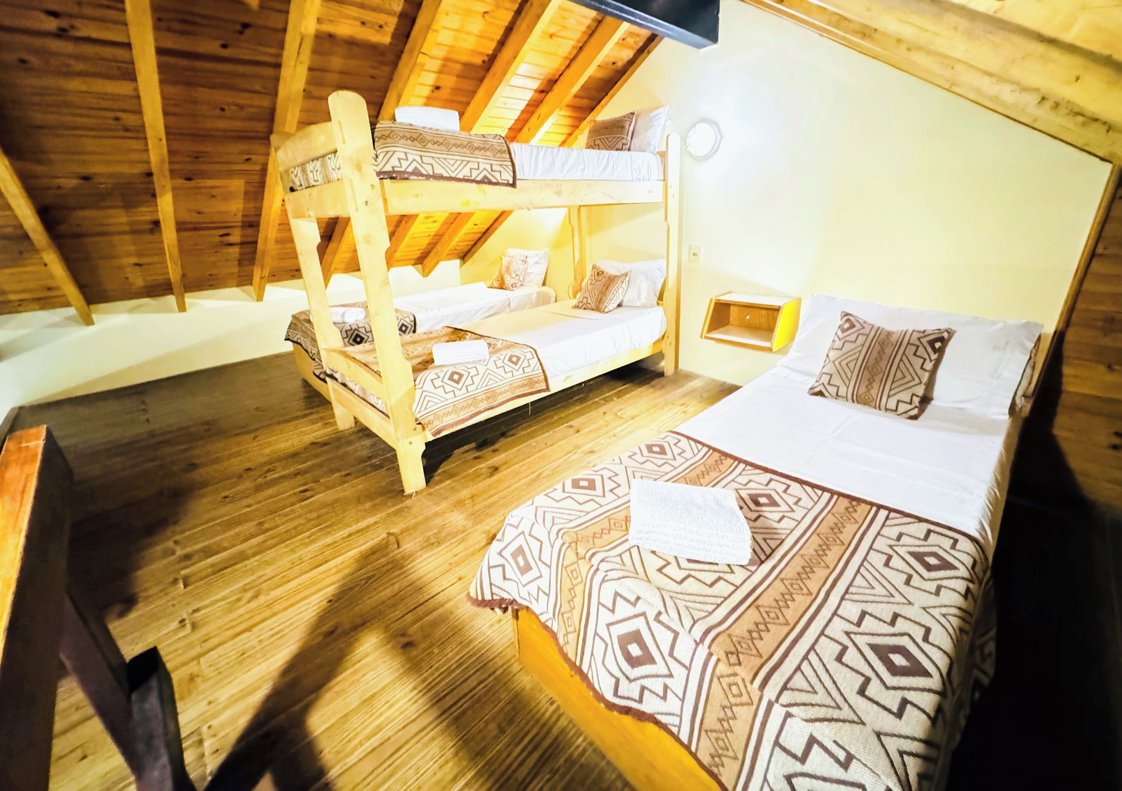 Habitación con dos literas de madera, colcha y almohadas estampadas, una mesita de noche con lámpara y suelo de madera.