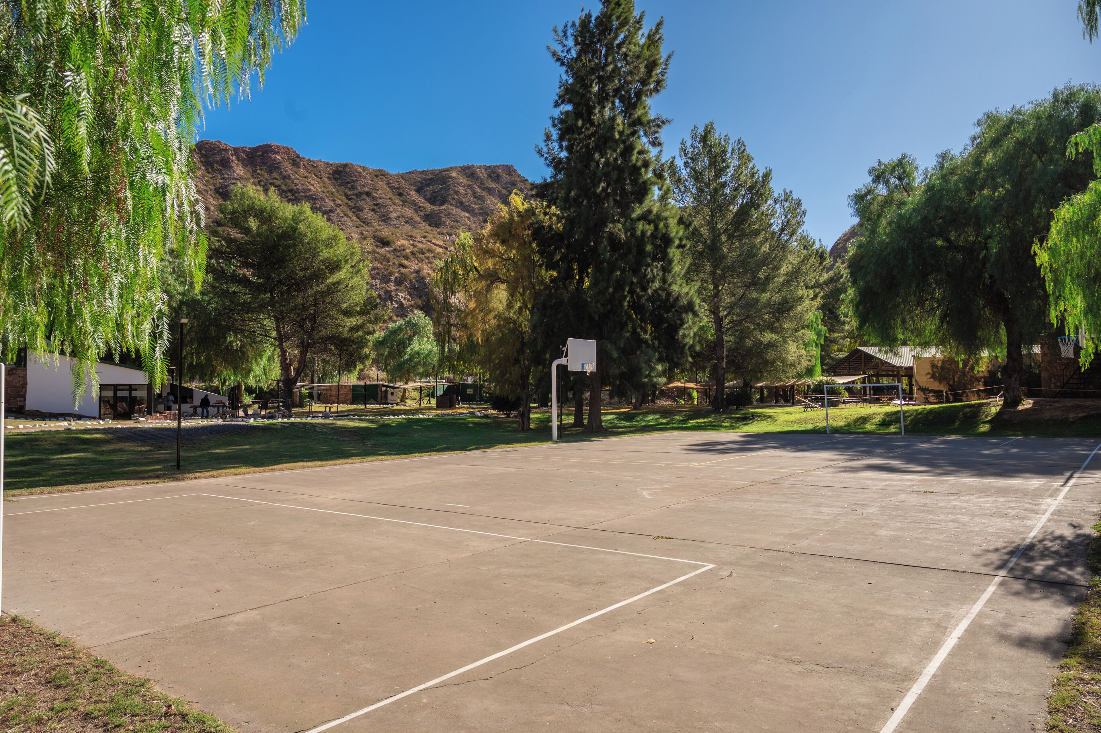 Una cancha de baloncesto al aire libre con cielo despejado, árboles y una montaña al fondo.