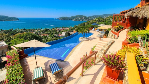 Un área de piscina con vista al mar, sillas de descanso y plantas en macetas.