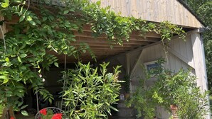 En träbyggnad med en överbyggd veranda, krukväxter och en hängande blomkorg.