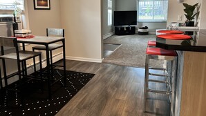 A modern kitchen with a dining area, a large TV, and a plant.