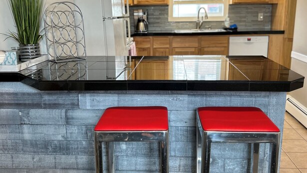 A modern kitchen with wooden cabinets, a black countertop, and two red bar stools.
