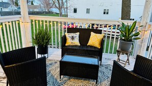 A covered outdoor seating area with wicker furniture, a patterned rug, and potted plants.