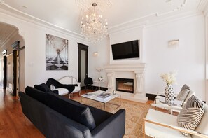 A spacious living room with a chandelier, a fireplace, a flat-screen TV, and modern furniture.