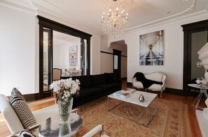 A spacious living room with a black sofa, a white armchair, a coffee table, and a chandelier.