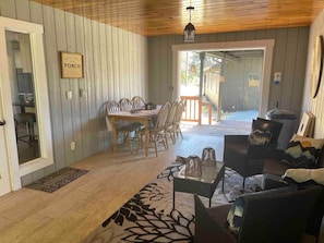 A cozy room with a wooden ceiling, a dining table with chairs, a sofa, and a patterned rug.