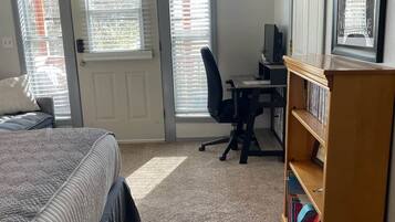 A bedroom with a bed, a desk, a chair, a bookshelf, and a door leading to a balcony.